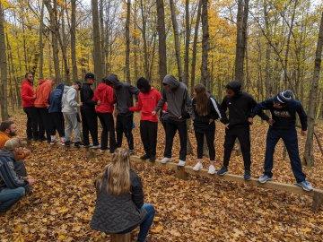 树林里的学生们手拉手站在一根圆木上.